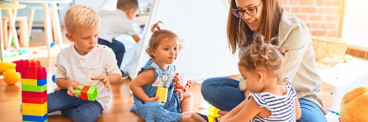 Beautiful teacher and group of toddlers playing around lots of toys at kindergarten Beautiful teacher and group of toddlers playing around lots of toys at kindergarten
