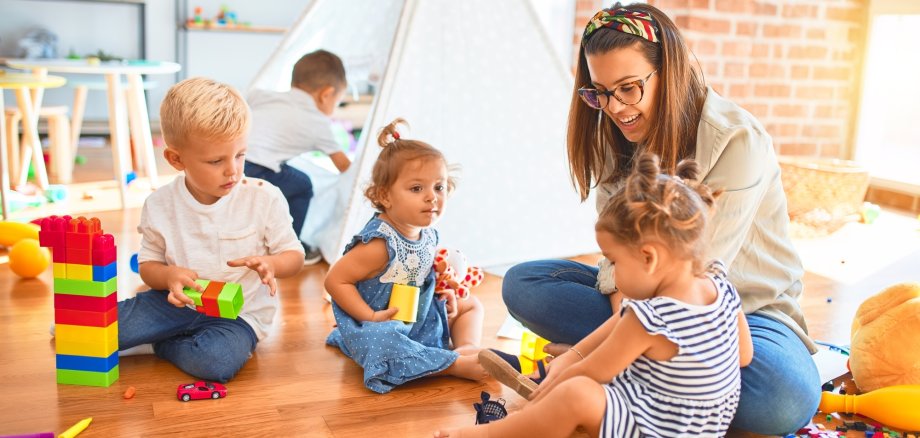 Beautiful teacher and group of toddlers playing around lots of toys at kindergarten