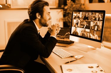 Successful positive Caucasian business man in a suit, sits at a workplace in the office, negotiating with partners on a video conference using a computer, discussing new project, terms of cooperation