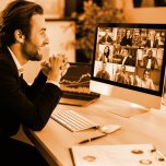 Successful positive Caucasian business man in a suit, sits at a workplace in the office, negotiating with partners on a video conference using a computer, discussing new project, terms of cooperation