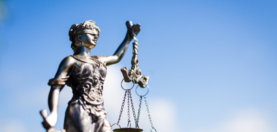 Helle Statur der Justitia vor einem blauen Himmel.