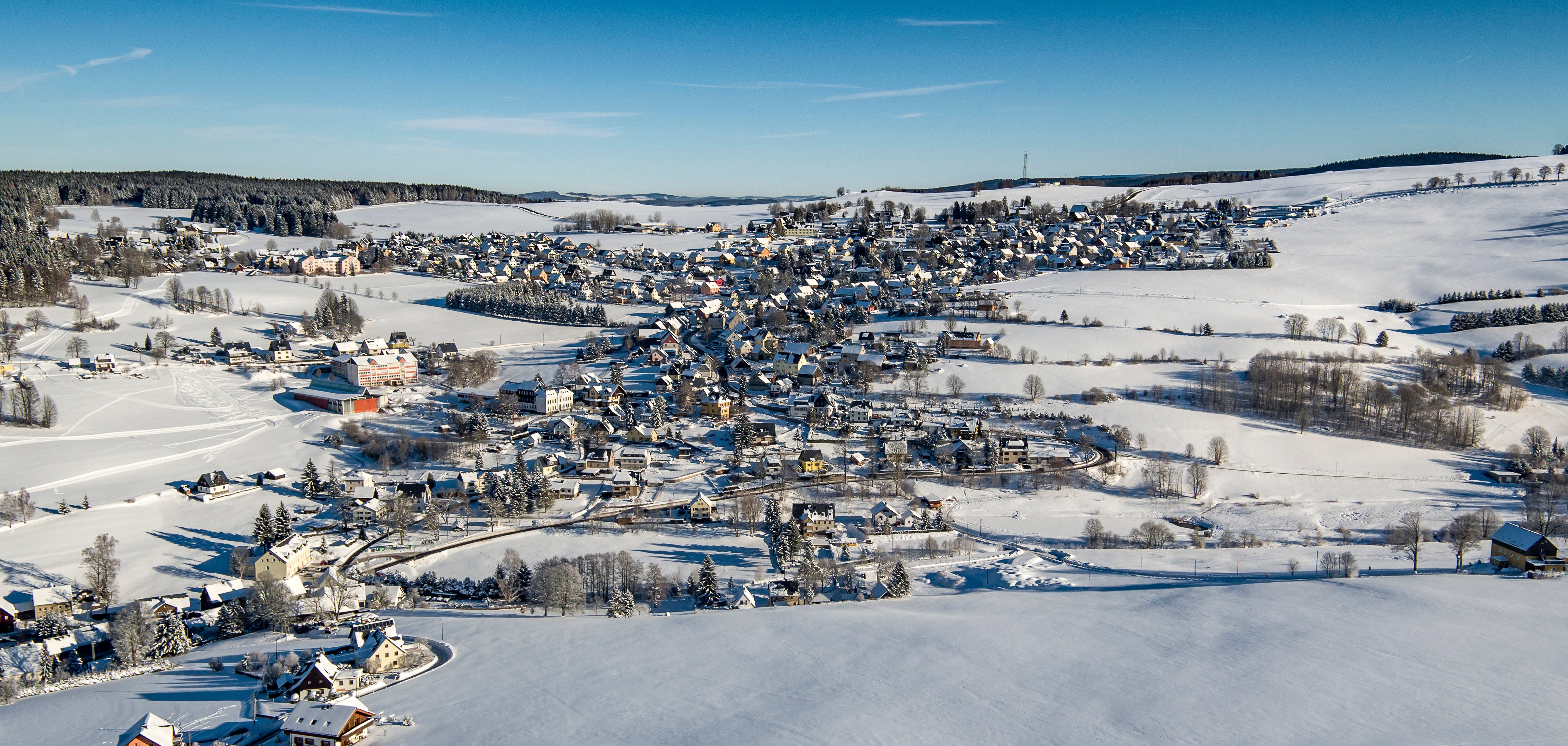 Zusehen ist die sächsische Gemeinde Breitenbrunn als Luftbild in einer winterlichen Landschaft mit reichlich Schnee und blauem Himmel.