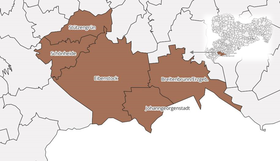 Zu sehen ist eine Landschaftsaufnahme der Kommune Breitenbrunn im Erzgebirge. Die Landschaft ist hügelig und verschneit. In der verschneiten Landschaft stehen mehrere Baumgruppen, der Himmel ist klar und blau. 